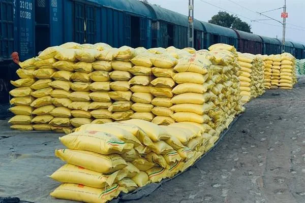 रेल मालगाड़ियों के पास कतारों में रखी पीले रंग की खाद की बोरियां